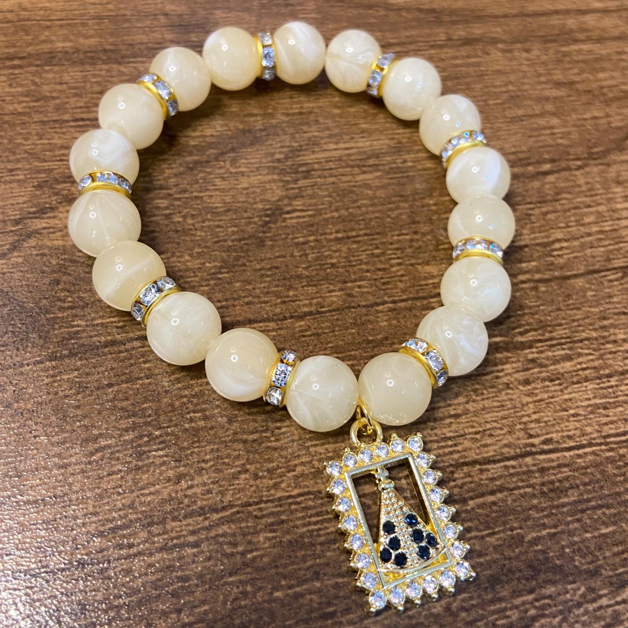PULSEIRA PÉROLA BEGE COM PINGENTE NOSSA SENHORA APARECIDA COM STRASS 08MM  (03 UNIDADES)